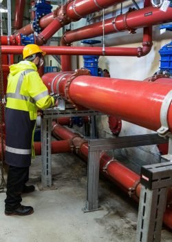 Engineer with safety gear inspecting red industrial piping system indoors.